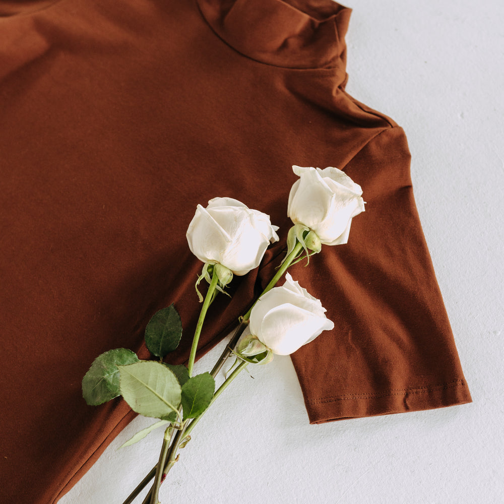 Augustine Top flatlay on white background with white roses laid on top.