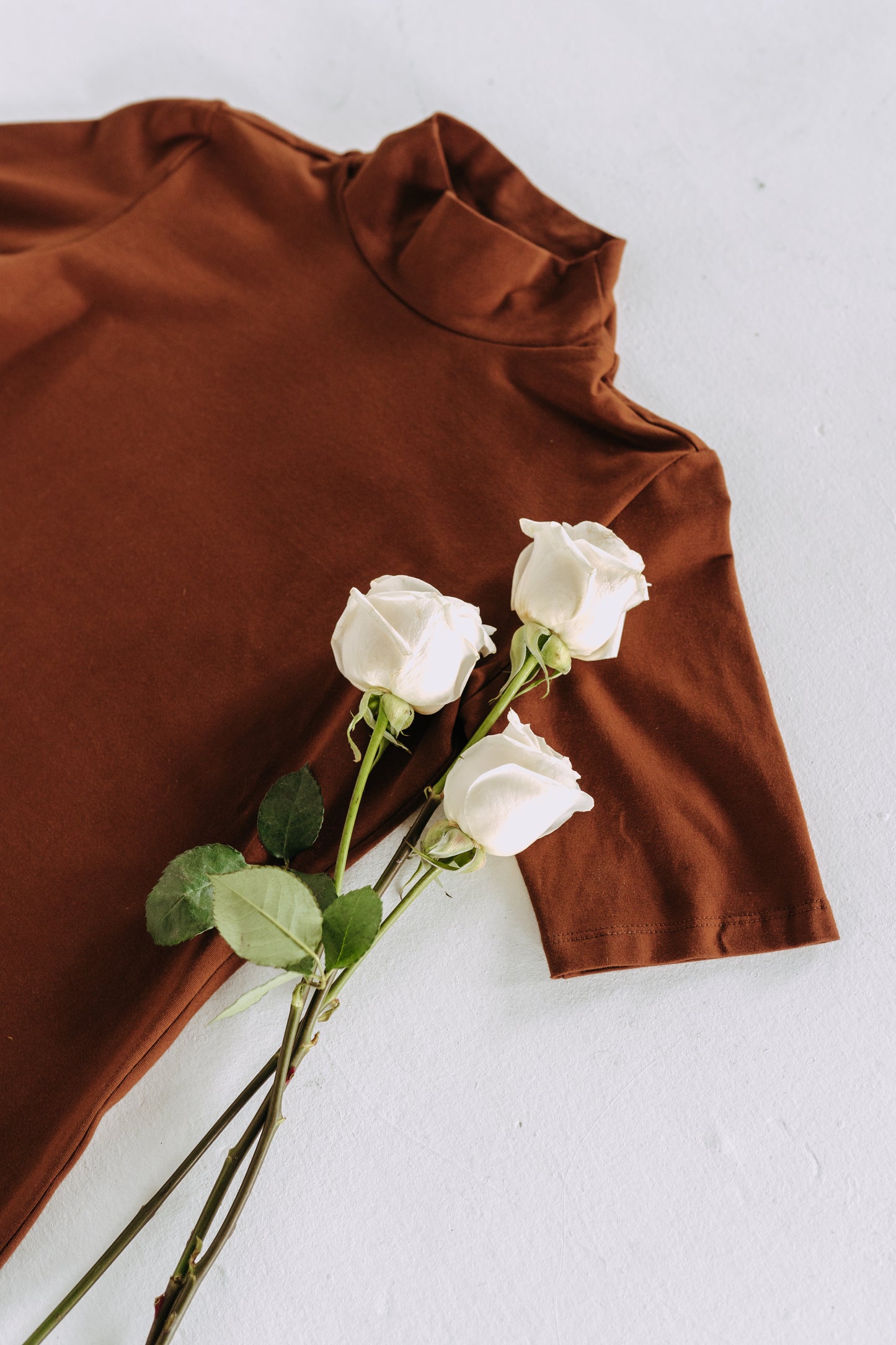 Augustine Top flatlay on white background with white roses laid on top.